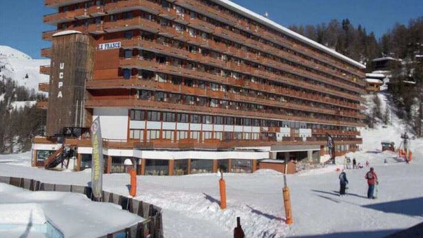 Et hotel med flere etager, altaner, en stolelift og et sneklædt bjerg i baggrunden.