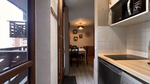 Une cuisine étroite équipée d’un lave-vaisselle, d’un four à micro-ondes et d’un plan de travail en bois. On aperçoit un coin repas avec une table et des chaises à travers une porte ouverte.