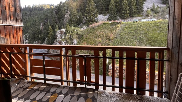 Un balcon en bois offrant une vue sur une colline boisée et une rivière.