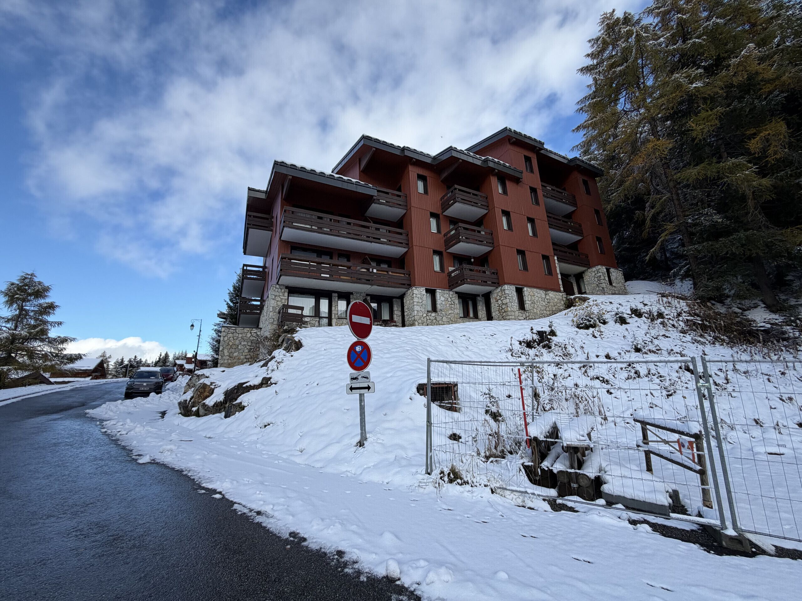 Un edificio de varios pisos con balcones, un letrero de no estacionamiento y una pendiente cubierta de nieve.