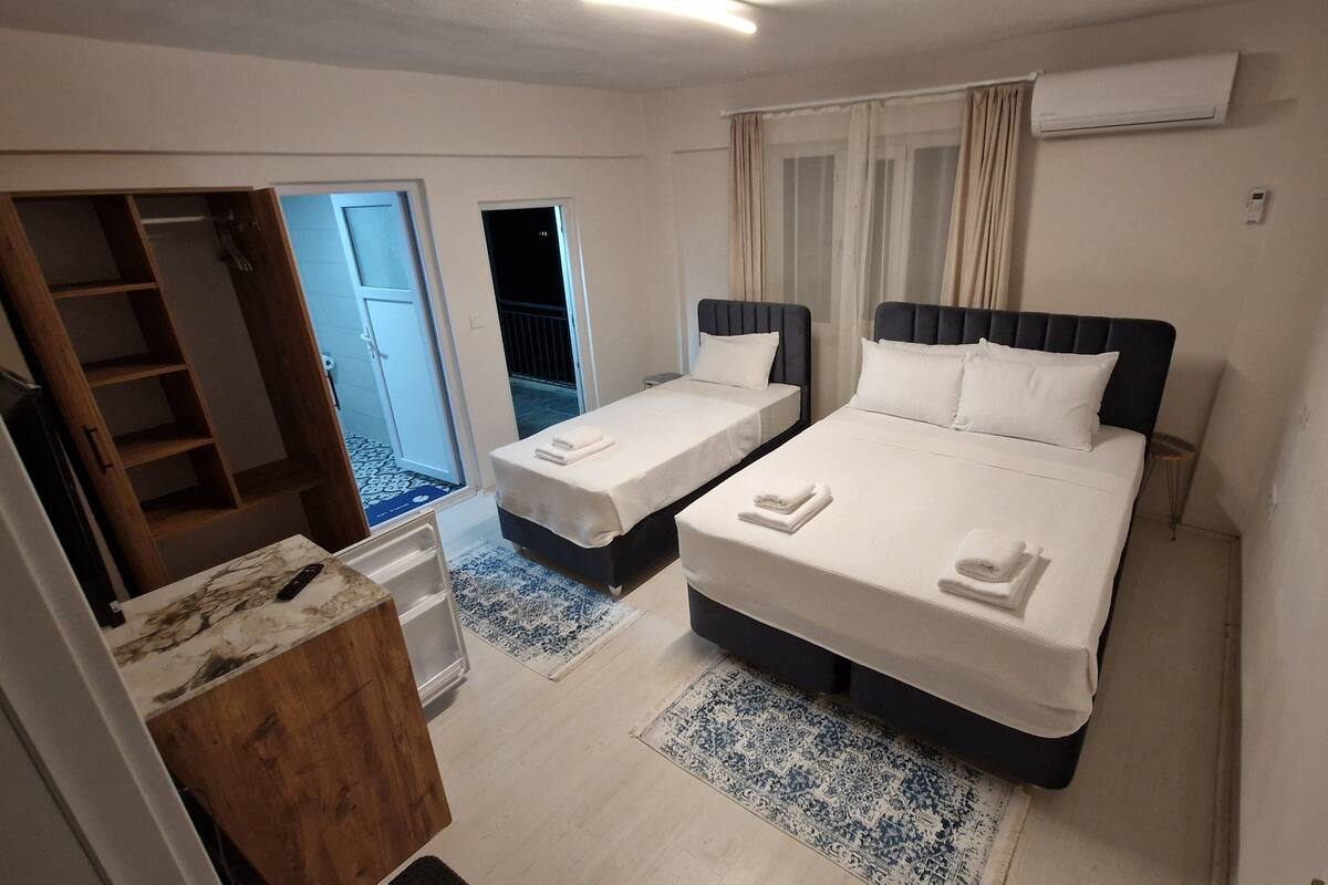 A hotel room with two single beds, a wooden wardrobe, a small desk, and a bathroom visible through an open door.