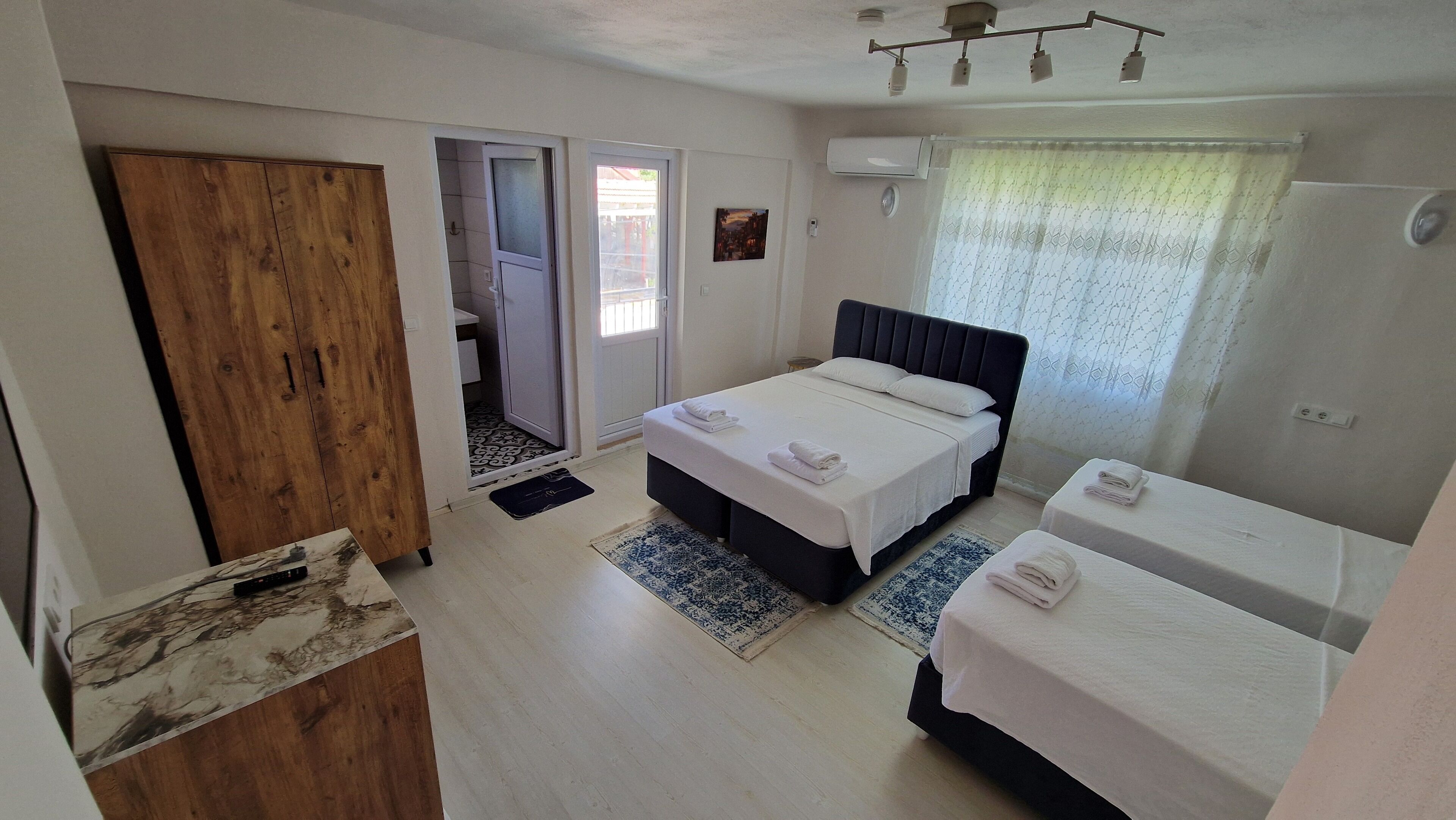 Habitación de hotel con cama, una mesita, armario y baño a la vista, visible a través de una puerta abierta.