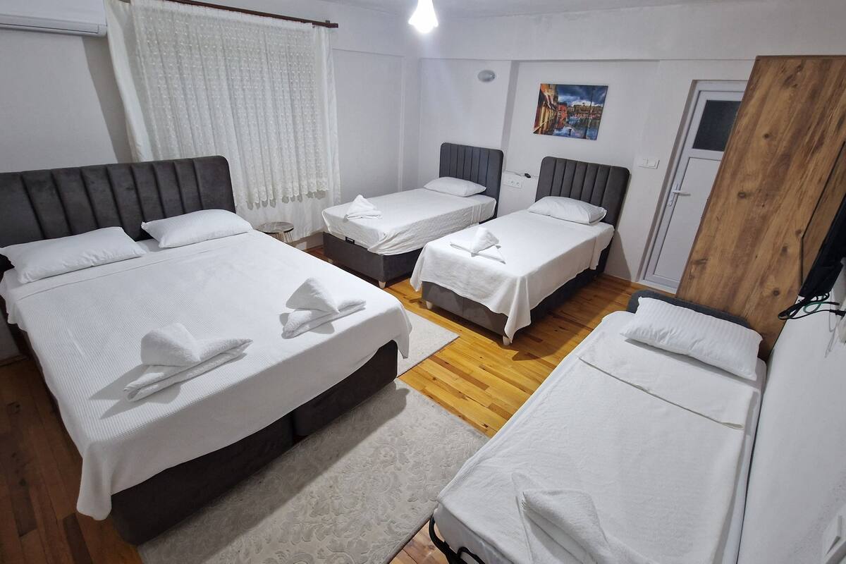 A hotel room with three beds, a wooden floor, a painting on the wall, and a door.