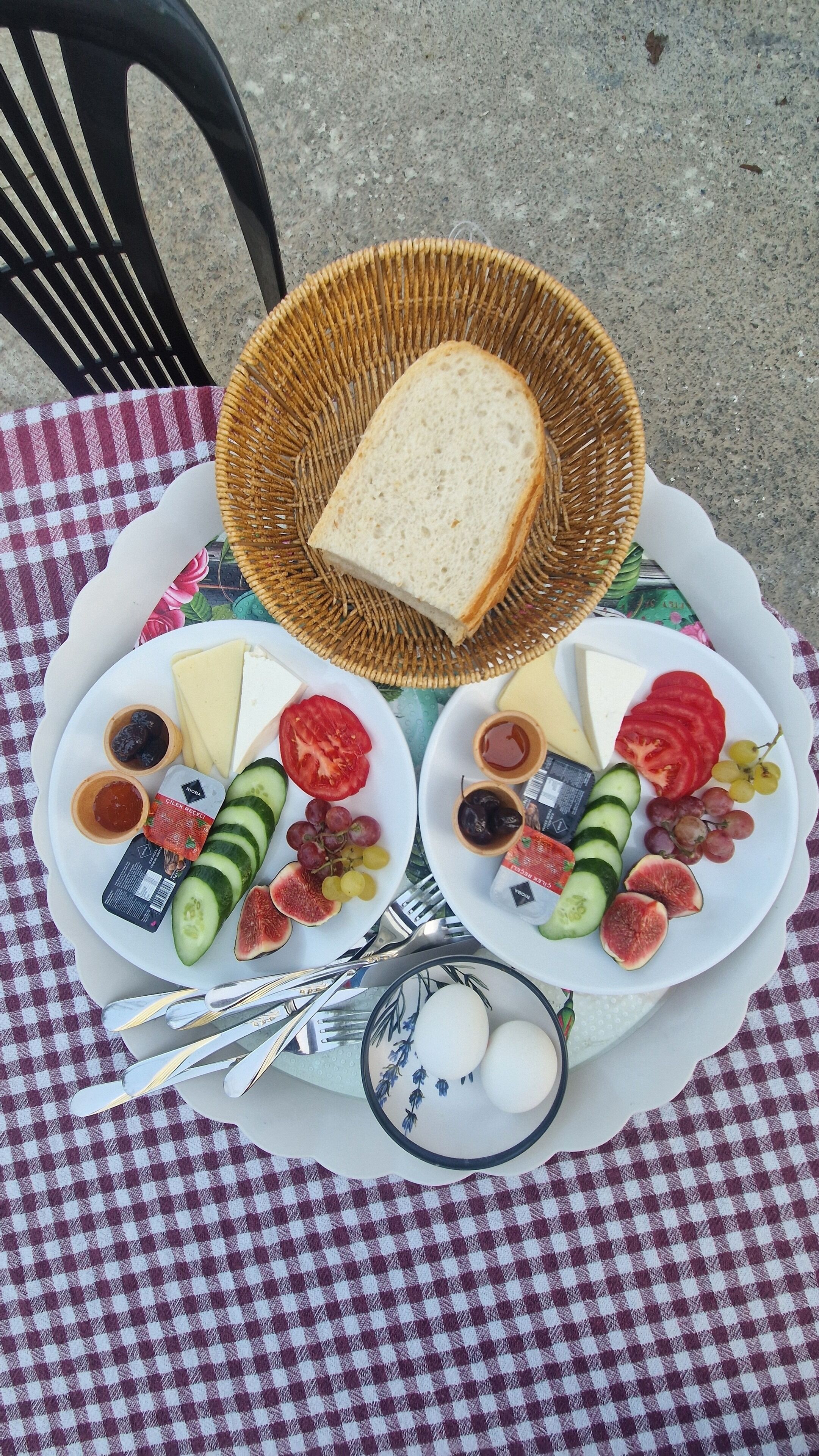 A checkered tablecloth with a plate of food, including cheese, grapes, and vegetables, and a wicker basket with bread.
