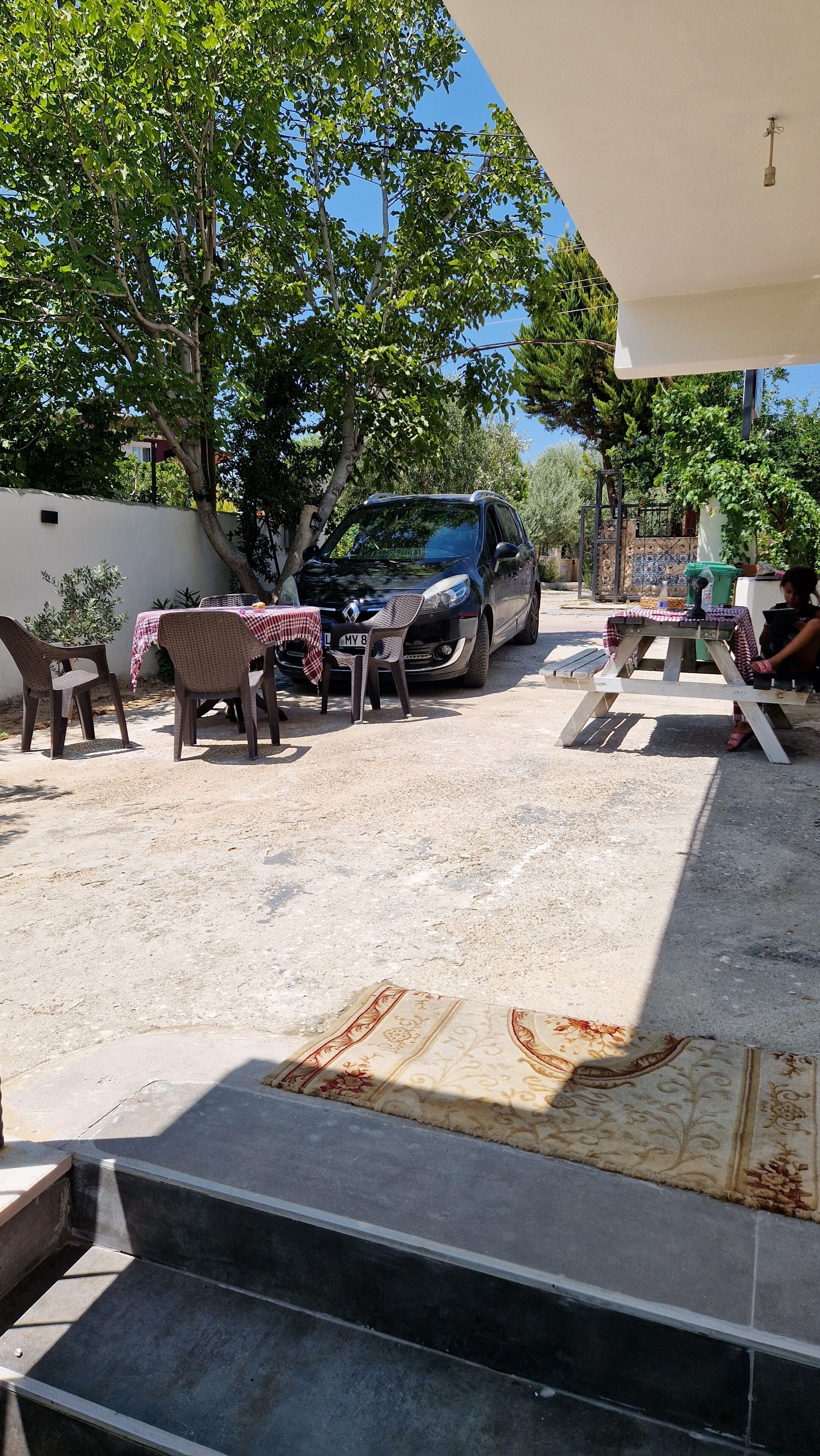 Un área de estar al aire libre con una mesa, sillas, un automóvil estacionado y una escalera que conduce a un nivel superior.
