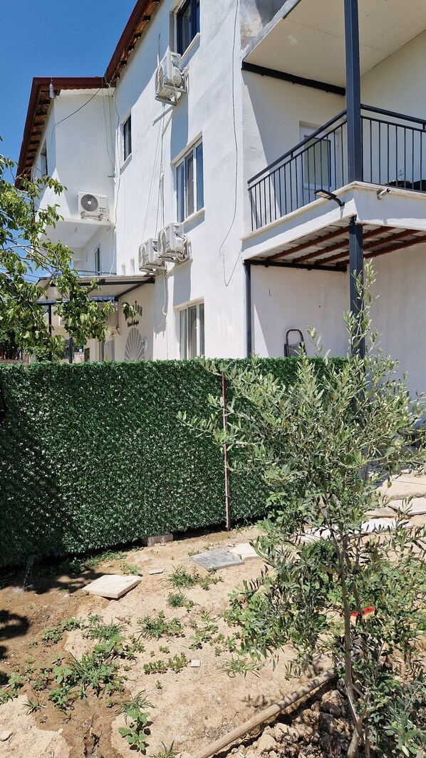 Un bâtiment à deux étages doté de climatiseurs, d’un balcon avec une rambarde en métal et d’une haie bien entretenue.