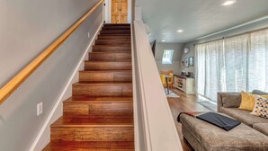 A staircase with wooden steps leading to a door, a living room with a sofa and a window, and a dining area with a table and chairs. - A-Frame of Mind - Secluded Escape  Hot tub (Rhododendron)