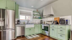 A modern kitchen with green cabinets, stainless steel appliances, and a window with blinds. - A-Frame of Mind - Secluded Escape  Hot tub (Rhododendron)