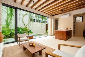 A modern living room with a wooden ceiling, a glass door leading to a pool, and a wooden dining table with a candle.