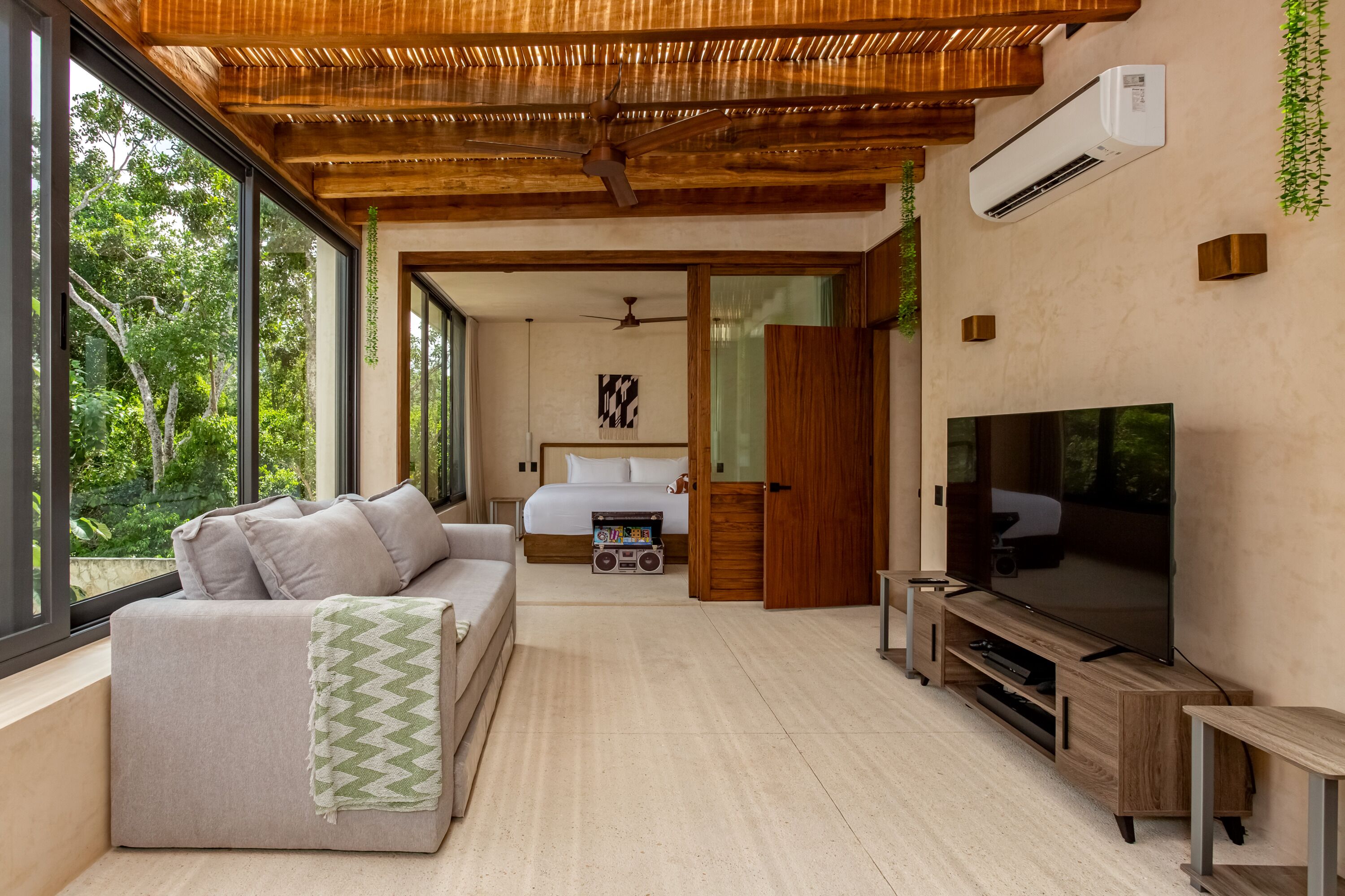 A modern room with a sofa, TV, and a bed with a view of greenery.