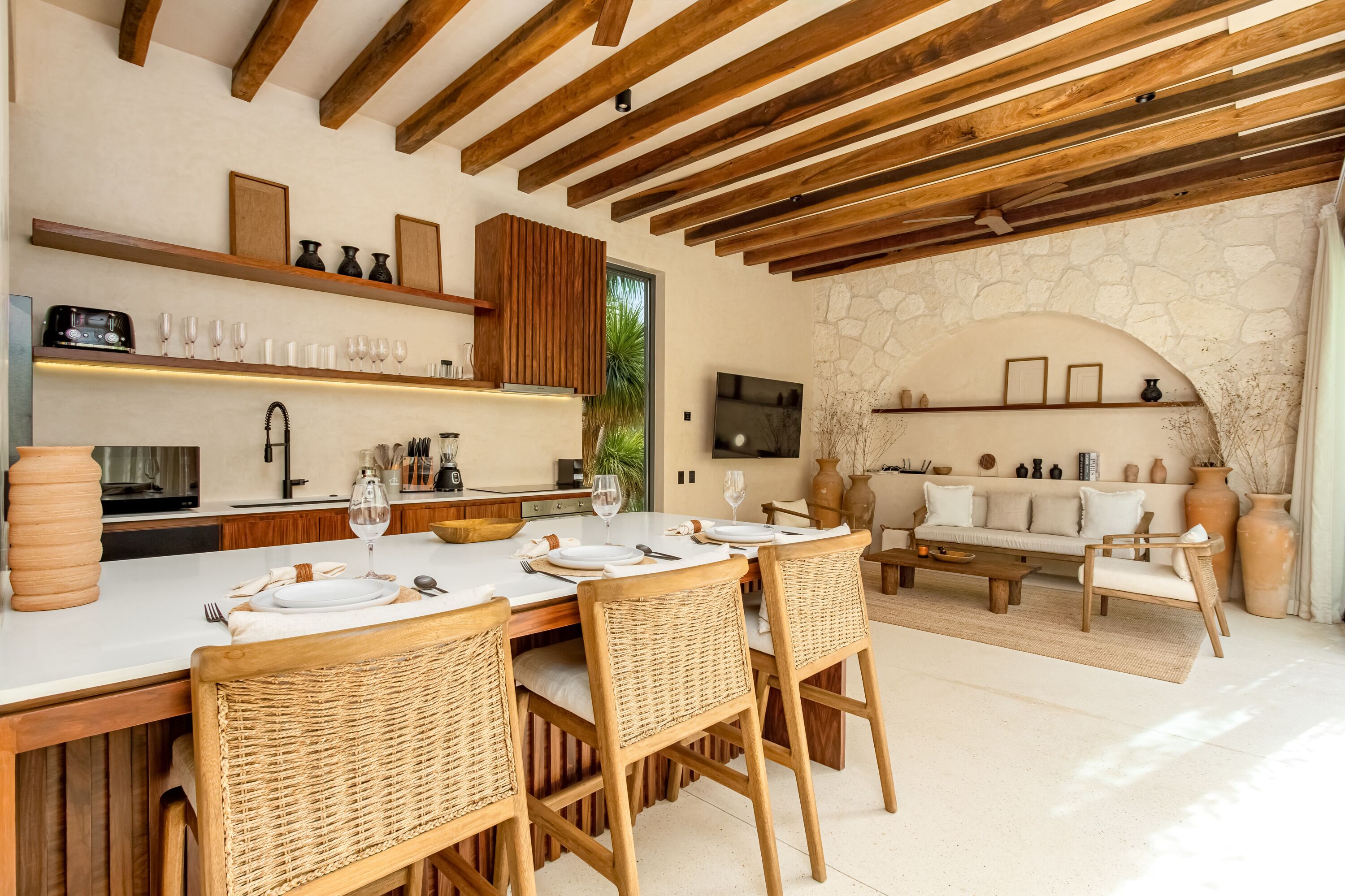 Una cocina moderna con vigas de madera, un comedor con sillas de mimbre y una pared de piedra.