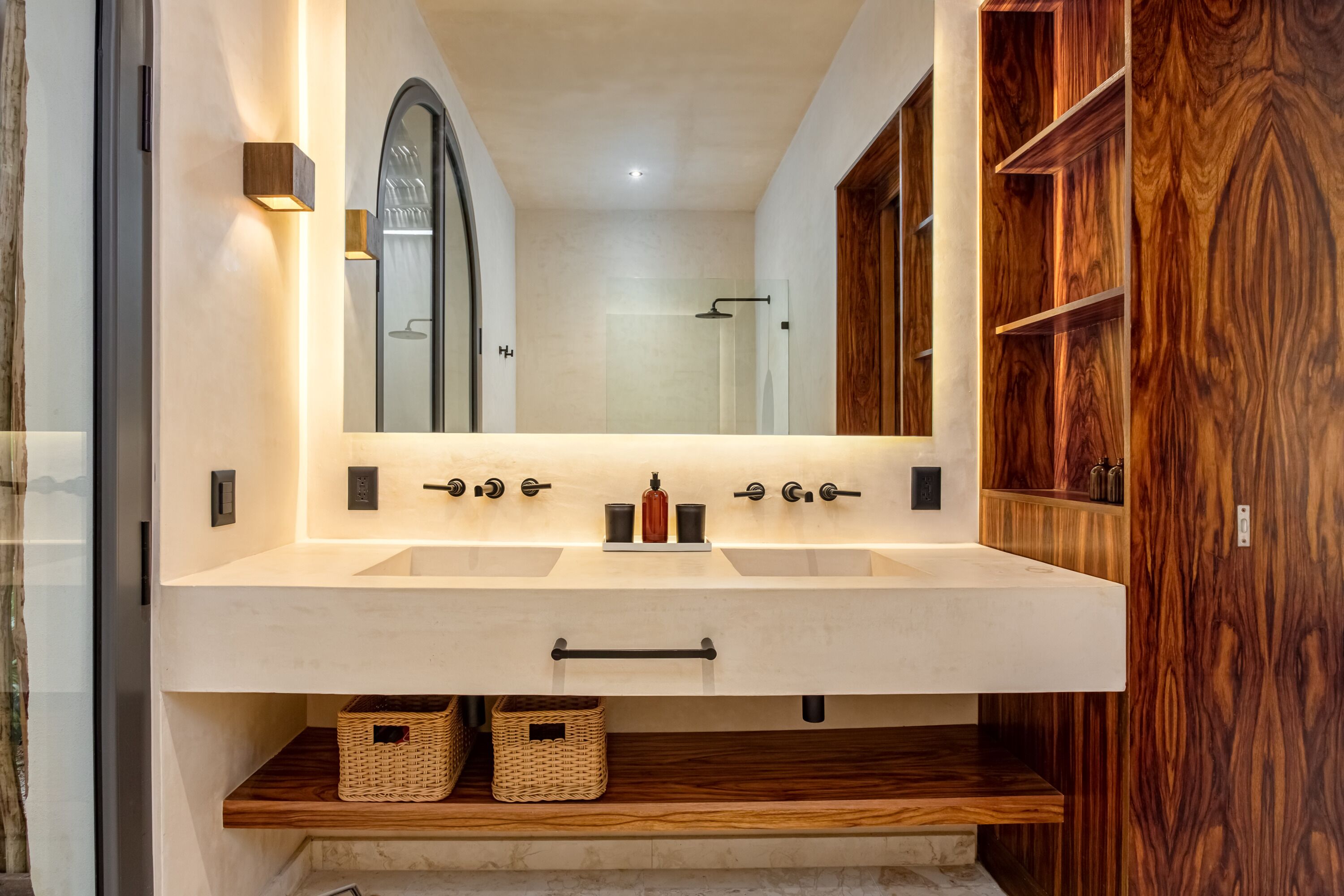 Un baño con un espejo grande, dos lavabos, estantes de madera y una puerta de madera.