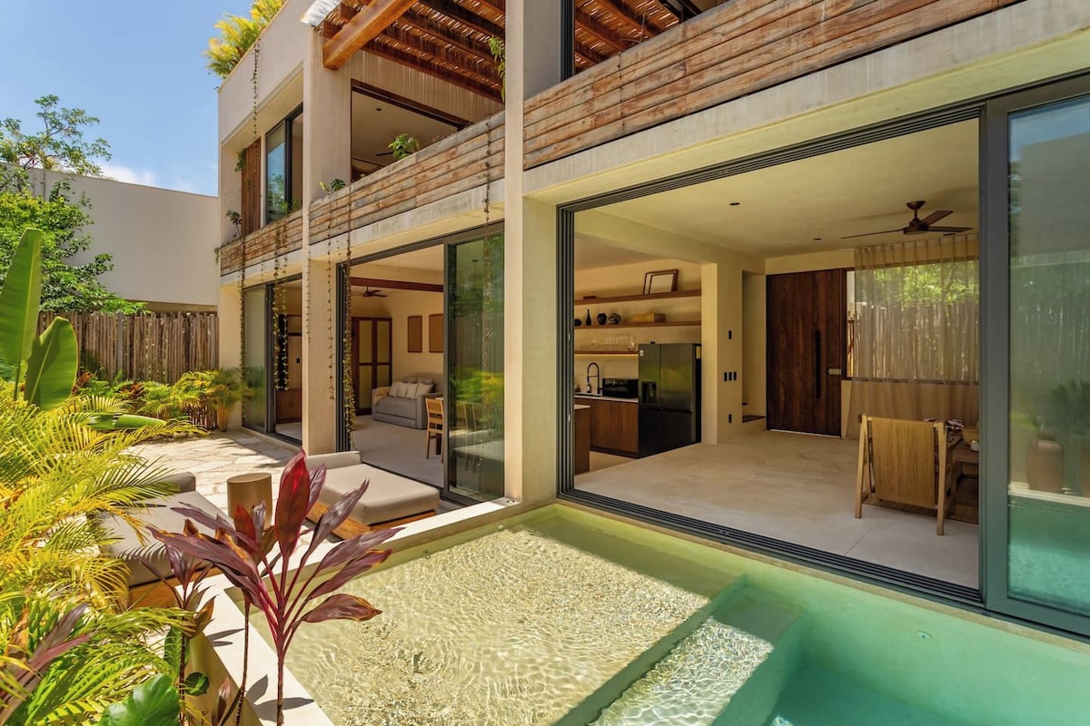 A modern two-story house with a glass-enclosed balcony, a small outdoor seating area, and a visible kitchen.