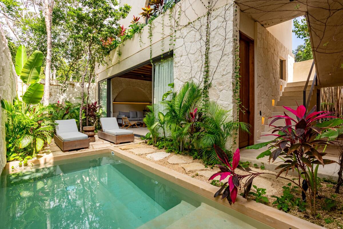 A pool area with lounge chairs, a stone wall, and lush greenery.