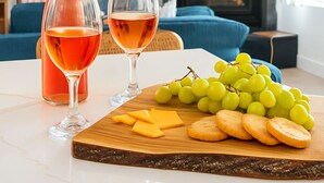 Une table à manger avec une bouteille de vin rouge, deux verres, une planche en bois sur laquelle on a disposé des raisins, du fromage et des crackers.