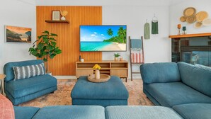 Un salon moderne doté d’un grand téléviseur à écran plat, de deux canapés bleus, d’un mur décoratif en bois et d’une image de plage tropicale affichée sur le téléviseur.