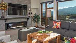 Una sala de estar moderna con chimenea, televisor grande y sofá con almohadones decorativos.