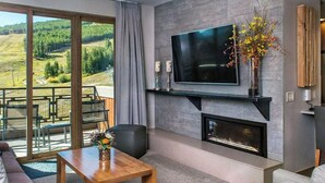 Una sala de estar moderna con chimenea, televisor de pantalla plana y vistas a un paisaje montañoso a través de grandes puertas correderas de vidrio.