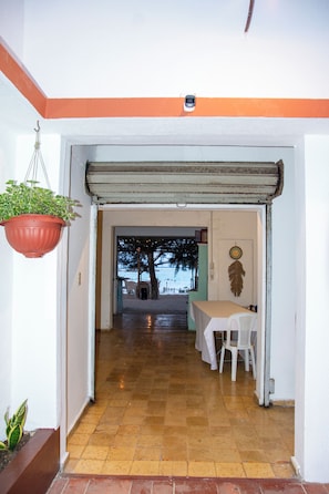 A hallway leading to a beach view with a table and chairs, a hanging plant, and a door with a feather decoration.