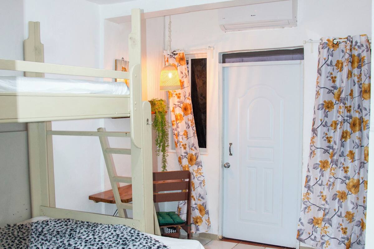 Una stanza con un letto a castello, una scrivania con una sedia, una porta e una tenda con motivo floreale.