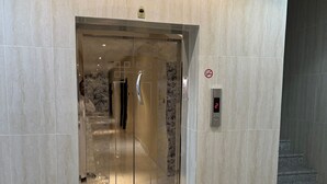 Un ascensor con una pantalla digital que muestra el número 2, un cartel de prohibido fumar y una pared con textura.