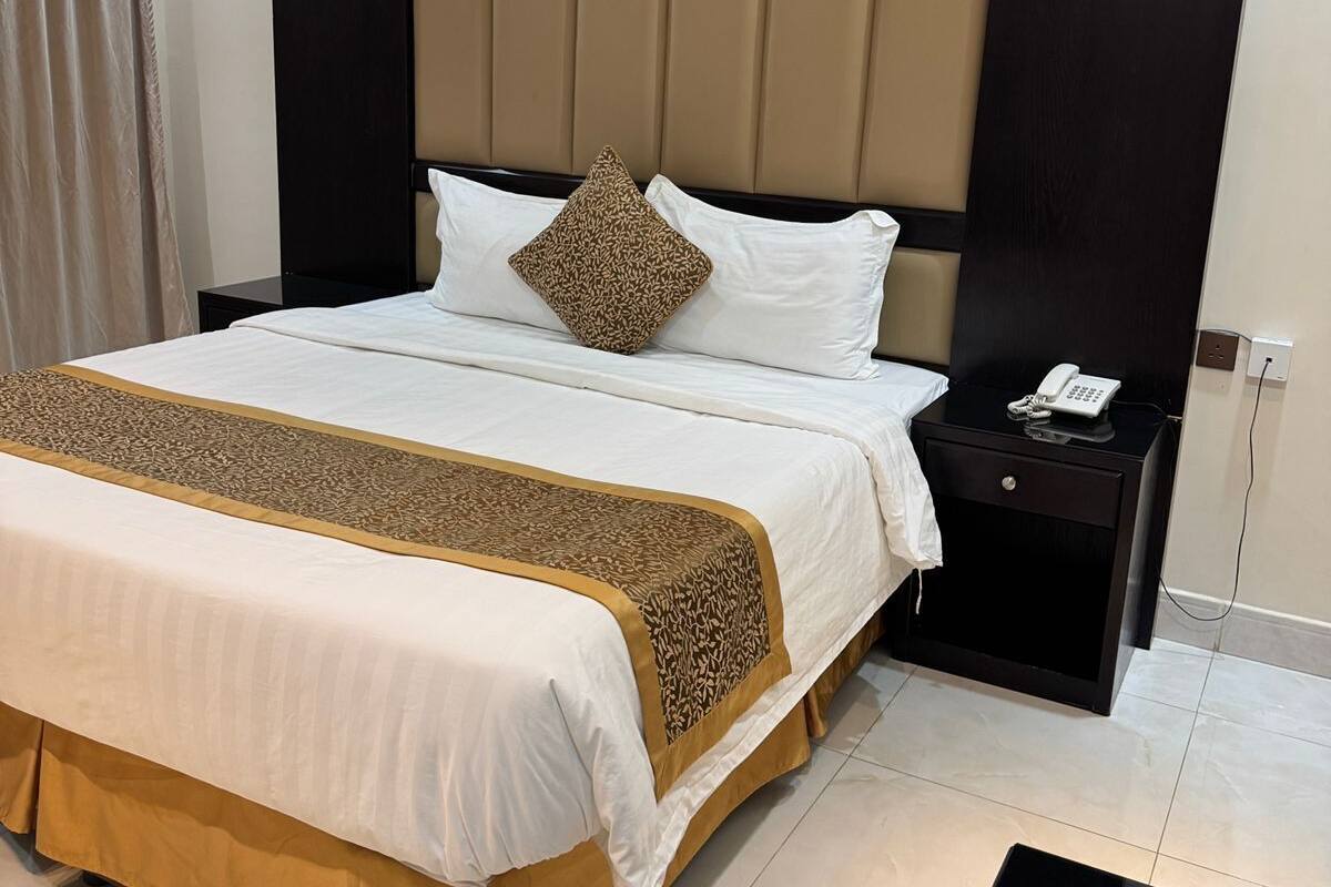 Moderni hotellihuone, jossa on suuri sänky, yöpöytä, jossa on puhelin, ja tumma yökaappi.