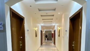 Un pasillo de hotel con una circulación central bordeada por puertas de madera, suelo de baldosas e iluminación empotrada.
