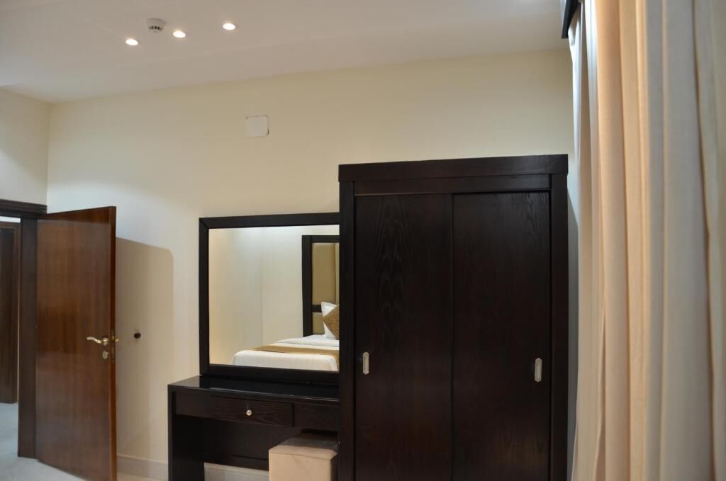 Una habitación de hotel con un espejo grande, un armario de madera y una mesita de noche.