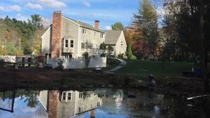 A two-story house with a brick chimney, a pond in front, and a pathway leading to the house. - Private, beautiful and quiet bedroom with private bathroom in county farmhouse.  (Norfolk)