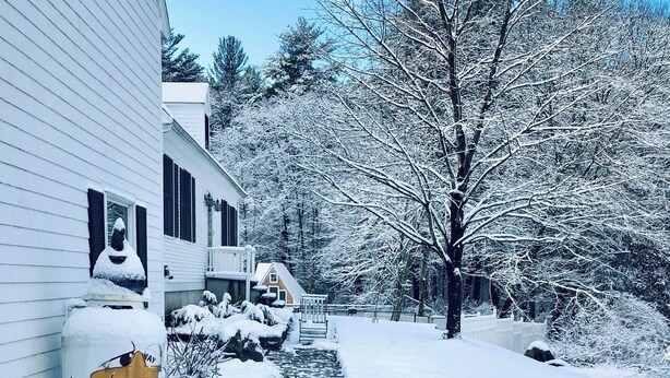A snow-covered pathway leading to a white house with a chimney, surrounded by trees and a small bridge. - Private, beautiful and quiet bedroom with private bathroom in county farmhouse.  (Norfolk)