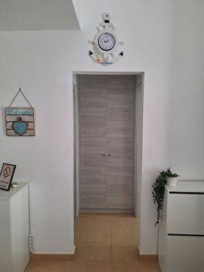 A hallway with a wooden door, a welcome sign, a clock, and a potted plant. - Casita Feliz Ftv (Antigua)