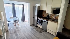 Eine kompakte Küche mit Kühlschrank, Backofen und Mikrowelle. Es gibt eine Essecke mit Tisch und Stühlen sowie ein großes Fenster mit Vorhängen.