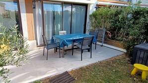 Ein Außenbereich mit einer Terrasse, einem Tisch, Stühlen, einem gelben Sessel, einem kleinen gelben Hocker und einem Blumentopf.