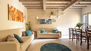 A living room with a sofa, a dining table, and a large painting on the wall. - San Cristofano Blu Apartment Florence (Florence)
