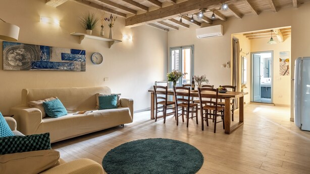 A spacious living room with a wooden ceiling, a dining area with wooden chairs and a table, and a large abstract painting on the wall. - San Cristofano Blu Apartment Florence (Florence)
