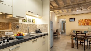 A modern kitchen with a gas stove, a sink, and a bowl of fruit on the counter. There is a dining area with a wooden table and chairs. - San Cristofano Blu Apartment Florence (Florence)