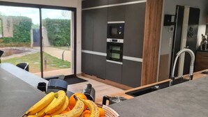 Une cuisine moderne équipée d’un four encastré, d’une machine à café et d’un ordinateur portable posé sur le plan de travail.