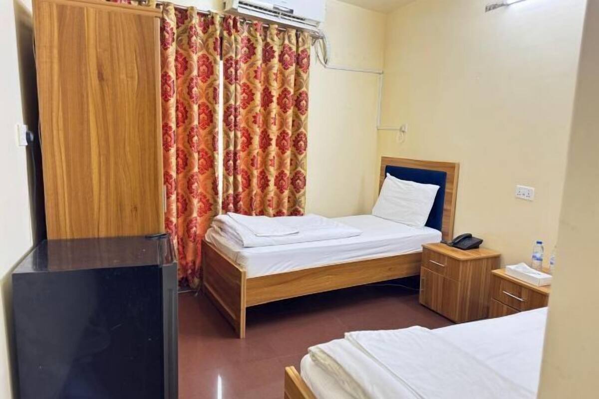 A hotel room with a wooden bed, a bedside table with a phone, a small wooden cabinet, and a curtain with a floral pattern.