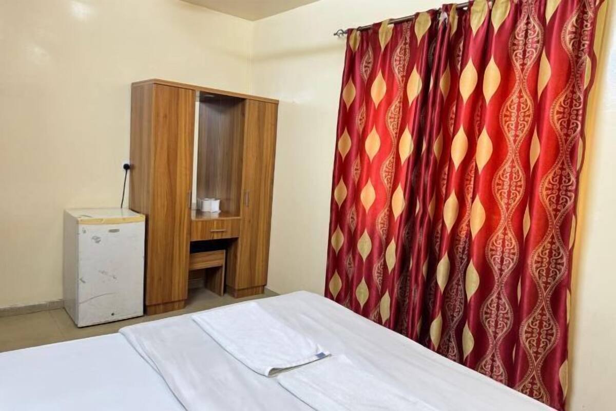 A room with a bed, a wooden wardrobe, a desk, and a patterned curtain.