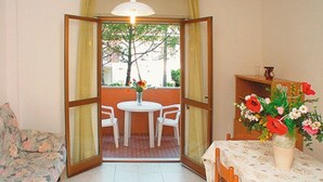 A room with a dining table and chairs, a sofa, and a window with curtains. - Have a nice stay in our well-equipped flat with balcony (Lignano Sabbiadoro)