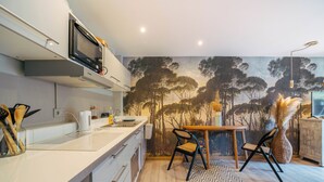 A modern kitchen with a microwave, toaster, and sink. There is a dining area with a table and chairs, and a mural of trees on the wall.