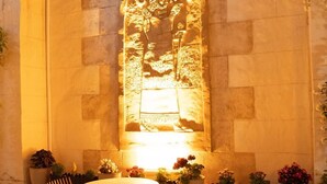 Un mur de pierre orné d’un bas-relief sculpté, une table ronde, deux chaises et des plantes en pot.