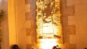 Un mur de pierre orné d’une sculpture en relief, deux chaises et des plantes en pot.