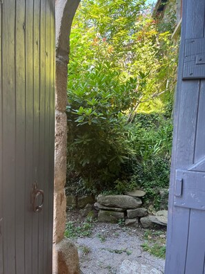 Un chemin de pierres menant à une porte en bois, entouré d’une végétation luxuriante et d’un mur de pierres.