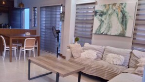Un soggiorno moderno con un tavolino in legno, un divano beige e un'area pranzo con un tavolo in legno e sedie bianche.