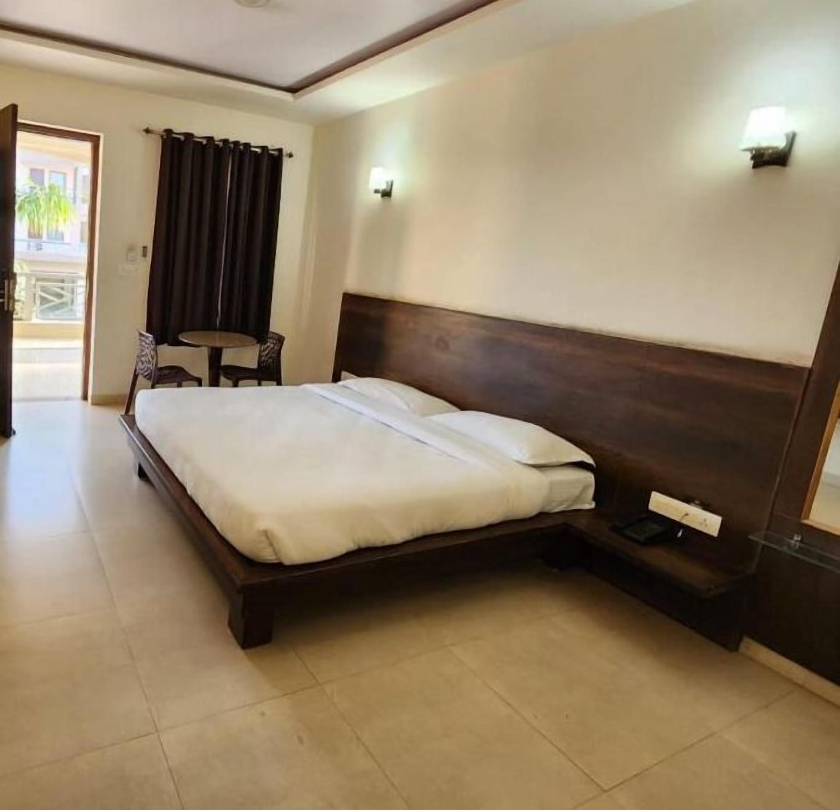 A hotel room with a large bed, a small table, a chair, and a view of the outside.
