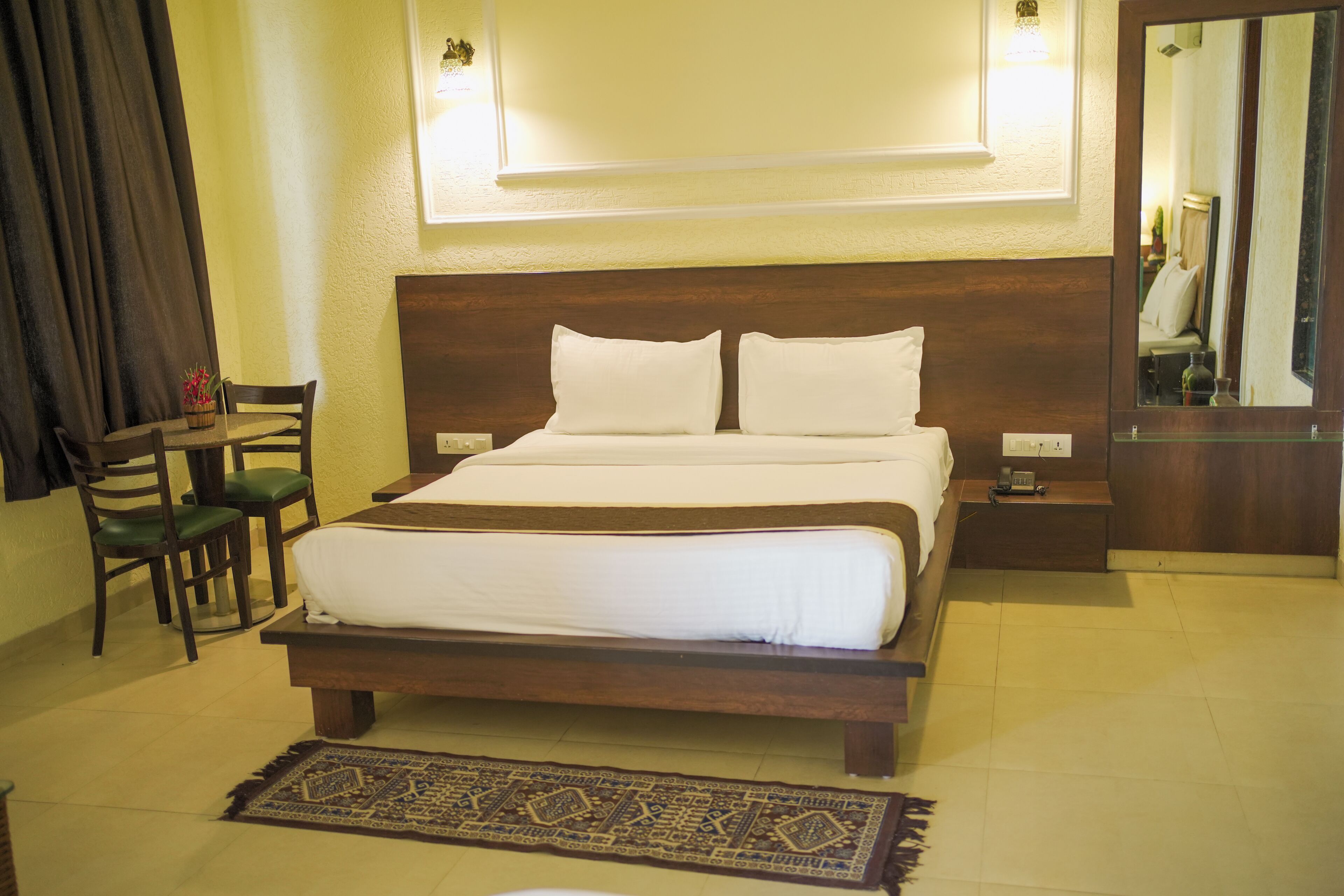 A hotel room with a bed, a desk, a chair, a rug, and a mirror.