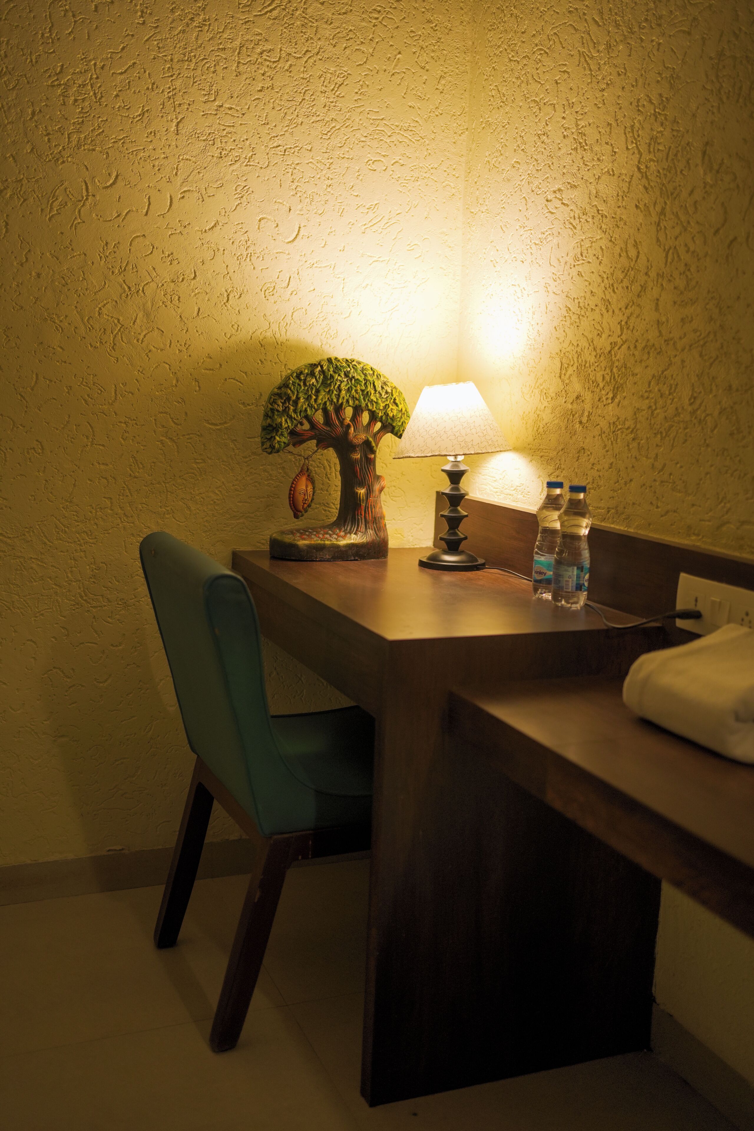 A wooden desk with a lamp, a small tree sculpture, and two water bottles.