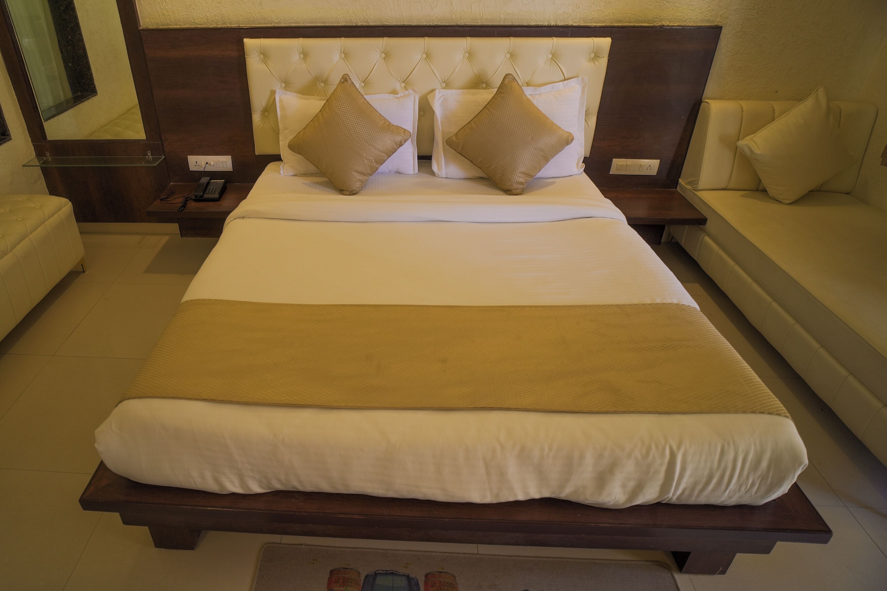 A hotel room with a large bed, bedside tables, a nightstand, and a sofa.