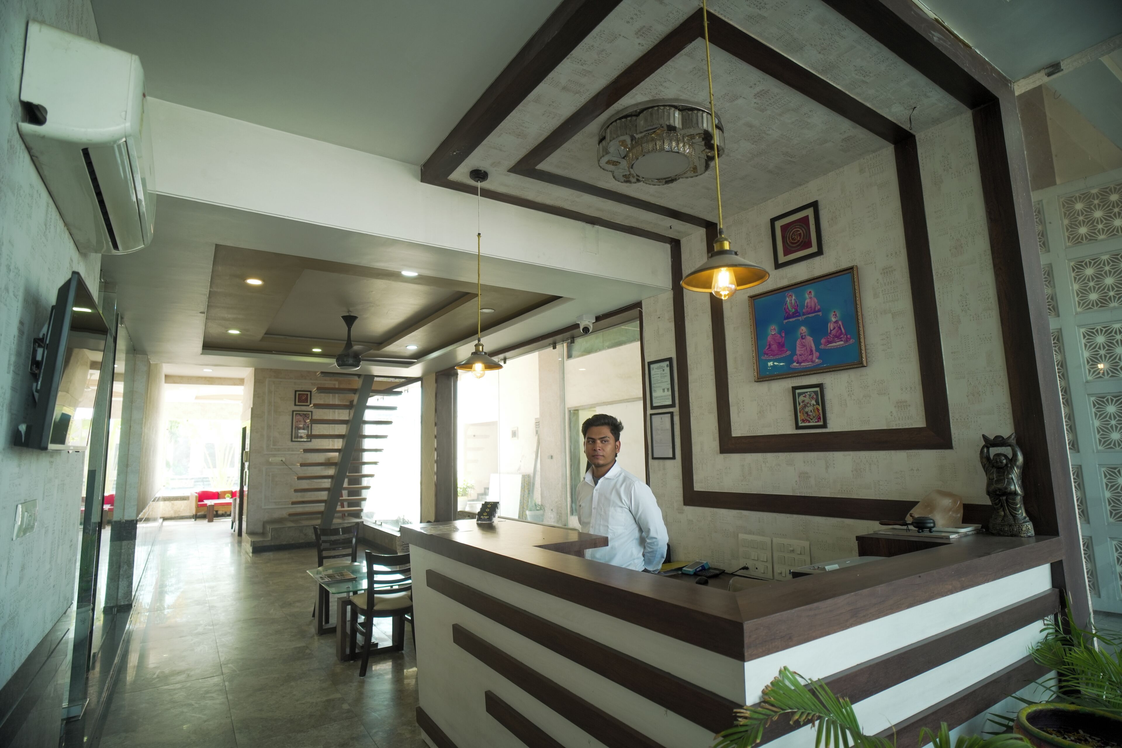 A hotel reception area with a receptionist, a reception desk, a staircase, and a dining area with tables and chairs.